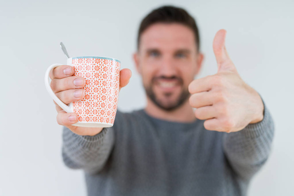 Young man driking cup of coffee over isolated background happy with big smile doing ok sign, thumb up with fingers, excellent sign - Foto, immagini