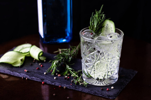Gin-tonic alcoholic cocktail. Cucumber, rosemary, ice. On a black wooden background. - Foto, Imagem