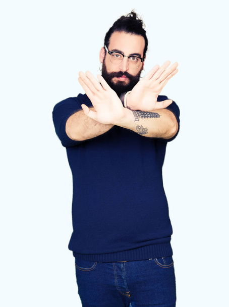 Young hipster man with long hair and beard wearing glasses Rejection expression crossing arms and palms doing negative sign, angry face - Foto, Imagem