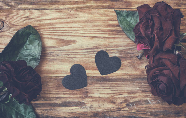 fondo del día de San Valentín, rosas secas oscuras y corazón negro en mesa de madera
 - Foto, Imagen