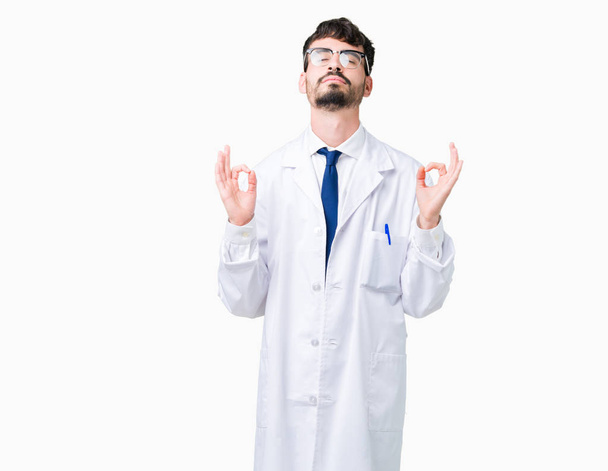 Young professional scientist man wearing white coat over isolated background relax and smiling with eyes closed doing meditation gesture with fingers. Yoga concept. - Foto, Imagem