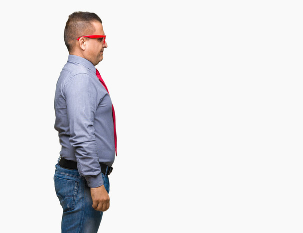 Hombre árabe de mediana edad que usa gafas rojas de moda sobre un fondo aislado mirando hacia un lado, pose de perfil relajado con cara natural con sonrisa confiada
. - Foto, Imagen