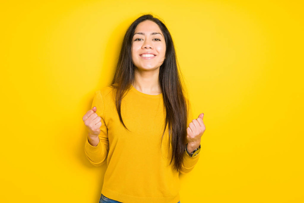 Beautiful brunette woman over yellow isolated background celebrating surprised and amazed for success with arms raised and open eyes. Winner concept. - Photo, image
