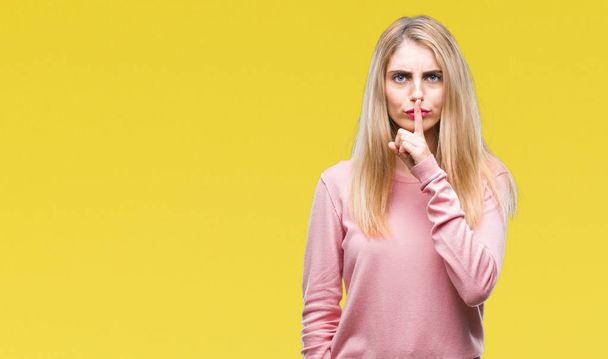 Young beautiful blonde woman wearing pink winter sweater over isolated background asking to be quiet with finger on lips. Silence and secret concept. - Foto, afbeelding