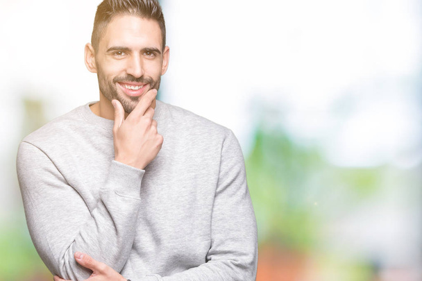 Young handsome man wearing sweatshirt over isolated background looking confident at the camera with smile with crossed arms and hand raised on chin. Thinking positive. - Photo, Image