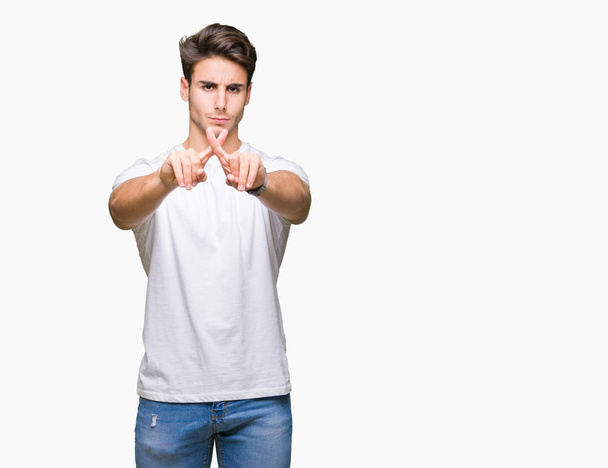 Jonge knappe man met witte t-shirt over geïsoleerde achtergrond afwijzing expressie kruising vingers doen minteken - Foto, afbeelding