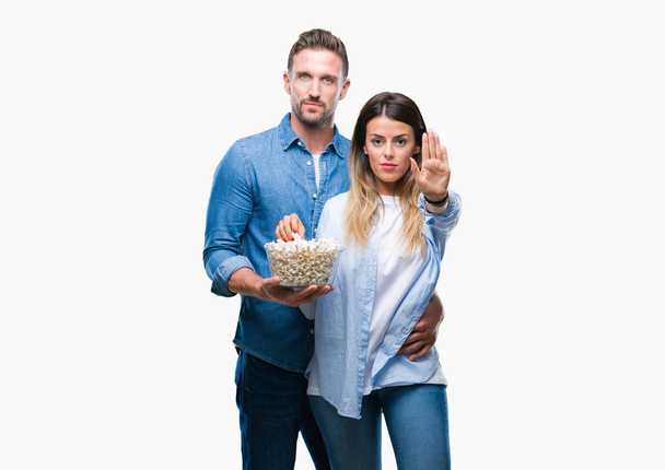 Young couple in love eating popcorn over isolated background with open hand doing stop sign with serious and confident expression, defense gesture - Zdjęcie, obraz