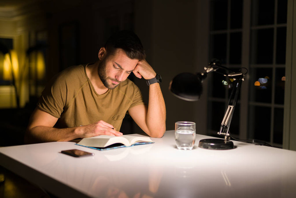 Joven hombre guapo estudiando en casa, leyendo un libro por la noche
 - Foto, imagen