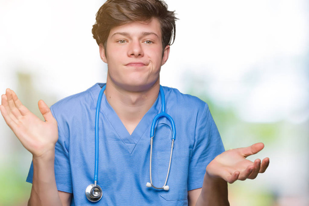 Jonge dokter medische uniform dragen over geïsoleerde achtergrond clueless en verward expressie met armen en handen aan de orde gesteld. Twijfel concept. - Foto, afbeelding