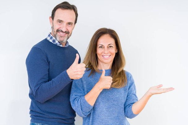 Beautiful middle age couple in love over isolated background Showing palm hand and doing ok gesture with thumbs up, smiling happy and cheerful - Foto, imagen