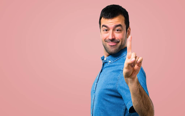 Hombre guapo con camisa azul contando el cartel número uno sobre fondo rosa
 - Foto, Imagen