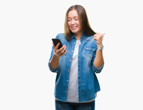 Young beautiful caucasian woman texting sending message using smartphone over isolated background screaming proud and celebrating victory and success very excited, cheering emotion - 写真・画像