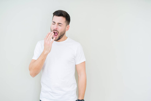 Young handsome man wearing casual white t-shirt over isolated background bored yawning tired covering mouth with hand. Restless and sleepiness. - Photo, Image