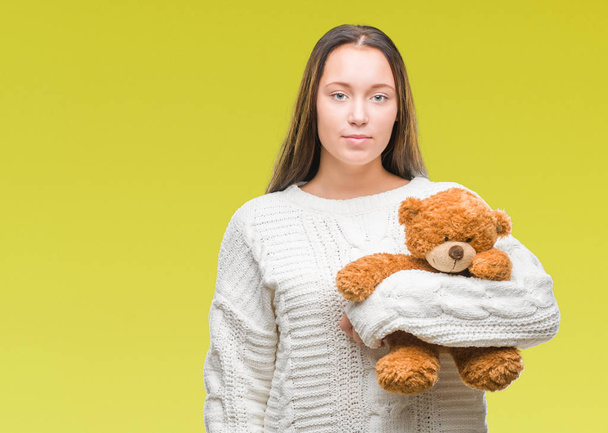 Young caucasian woman holding teddy bear over isolated background with a confident expression on smart face thinking serious - Φωτογραφία, εικόνα
