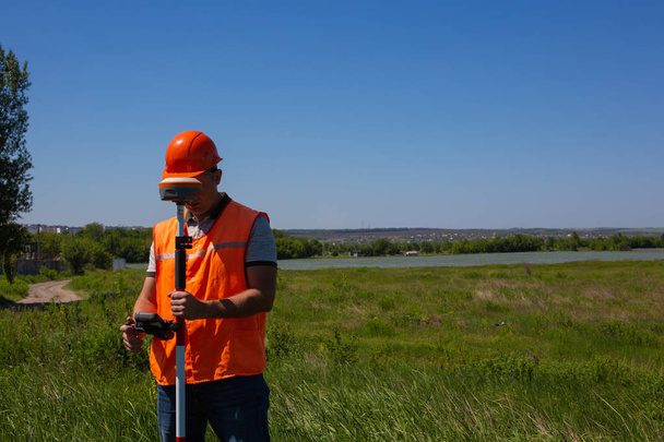 Профессиональный землемер измеряет наземный контрольный пункт с помощью GPS-ровера. Зеленое поле на заднем плане
 - Фото, изображение