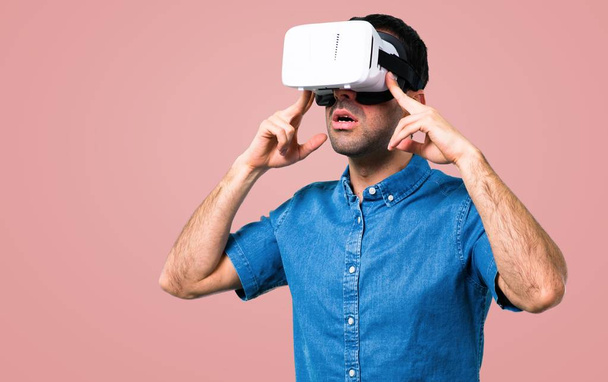 Handsome man with blue shirt using VR glasses on pink background - Фото, изображение