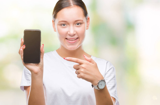 Молода красива біла жінка, що показує екран смартфона на ізольованому фоні дуже щаслива, вказуючи рукою і пальцем
 - Фото, зображення