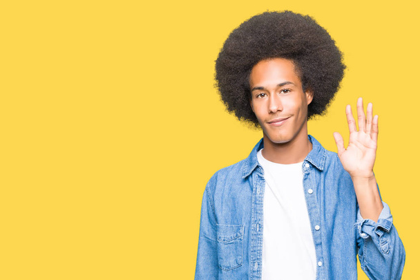junger afrikanisch-amerikanischer Mann mit Afro-Haaren, der darauf verzichtet, fröhlich und lächelnd Hallo zu sagen, freundliche Begrüßungsgeste - Foto, Bild