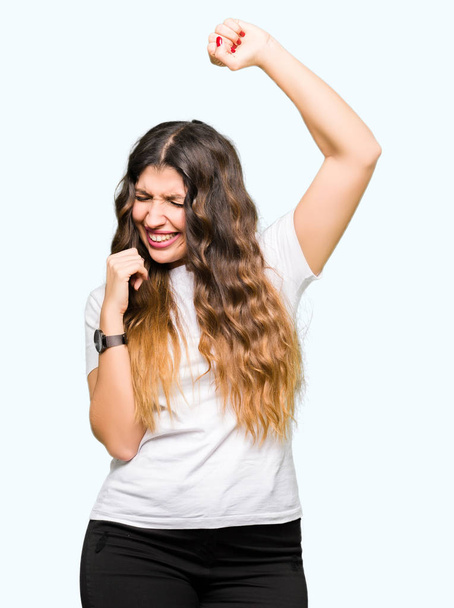 Young beautiful woman wearing casual white t-shirt very happy and excited doing winner gesture with arms raised, smiling and screaming for success. Celebration concept. - Foto, Bild