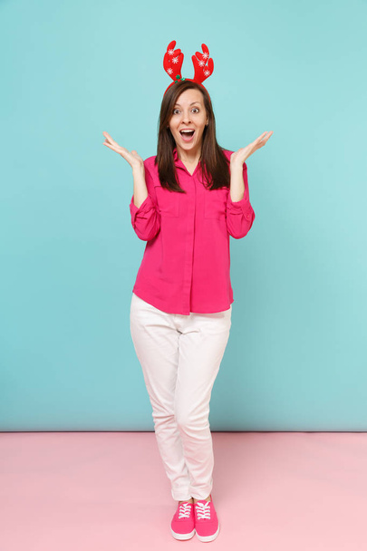 Полный портрет веселой молодой женщины в блузке из розовой рубашки, белых брюках, оленьих рогах, позирующих изолированно на ярко-розовой синей пастельной стене студии. Концепция модного образа жизни. Пространство для копирования
 - Фото, изображение
