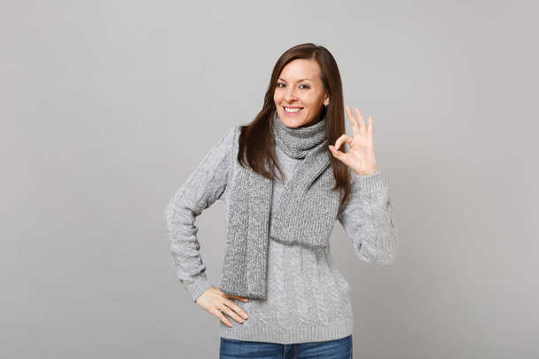 Smiling young girl in gray sweater scarf showing OK gesture isolated on grey wall background studio portrait. Healthy fashion lifestyle people sincere emotions cold season concept. Mock up copy space - Foto, Imagen