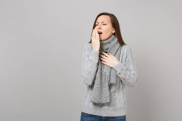 灰色のセーター マフラー、くしゃみ、灰色の壁の背景に分離の手のひらで覆って口を咳で若い女性。ライフ スタイル健康病気病気病気治療、寒い季節の概念。コピー スペースをモックアップします。 - 写真・画像