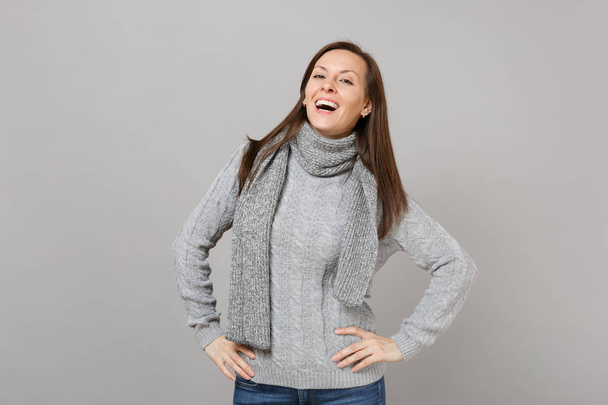 Charming young woman in gray sweater, scarf standing with arms akimbo isolated on grey background in studio. Healthy fashion lifestyle people sincere emotions, cold season concept. Mock up copy space - Fotografie, Obrázek