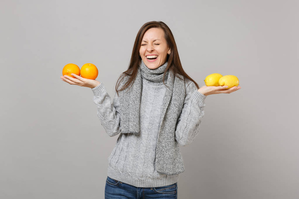 灰色のセーターで若い女性を笑いながら、目を閉じてスカーフ保持レモン オレンジ グレー背景に分離されました。健康ファッション ライフ スタイル人誠実な感情寒い季節のコンセプト。コピー スペースをモックアップします。 - 写真・画像