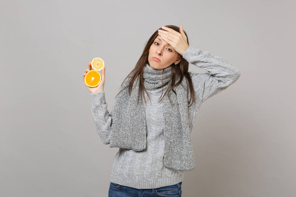 Giovane donna sconvolta in maglione grigio, sciarpa mettere mano sulla fronte, tenendo limone, arancio isolato su sfondo grigio. Stile di vita sano malato malattia trattamento, concetto di stagione fredda. Falsificare spazio di copia
 - Foto, immagini