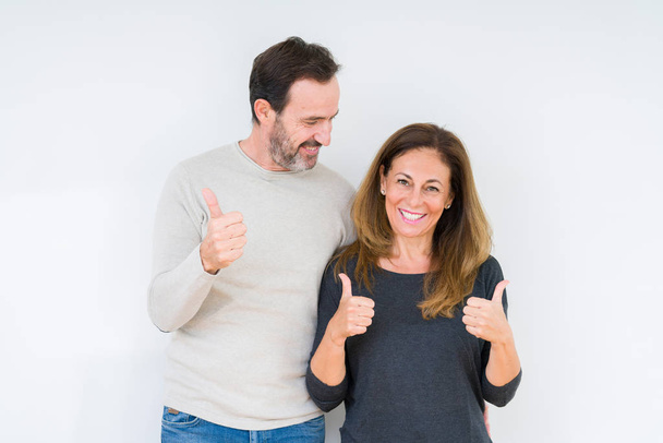 Beautiful middle age couple in love over isolated background success sign doing positive gesture with hand, thumbs up smiling and happy. Looking at the camera with cheerful expression, winner gesture. - Photo, Image