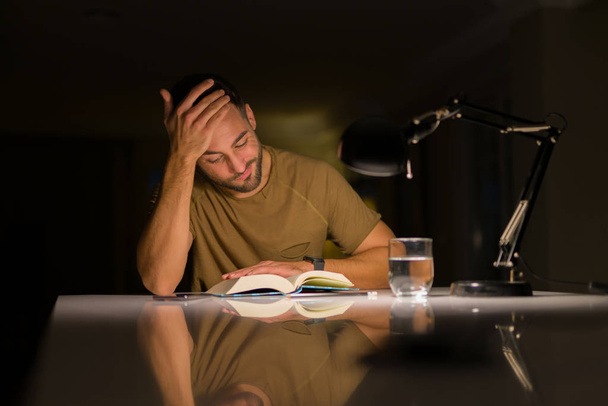 Jeune homme beau étudiant à la maison très ennuyé et stressant de lire un livre la nuit
 - Photo, image