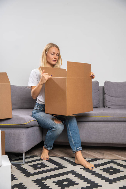 Image of young blonde with cardboard box sitting on sofa - Фото, зображення