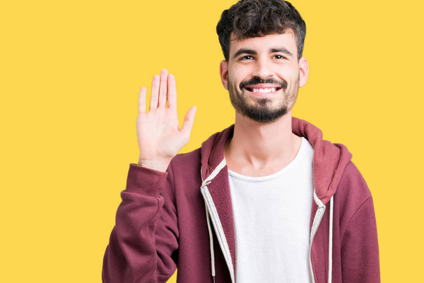 Young handsome man over isolated background Waiving saying hello happy and smiling, friendly welcome gesture - Photo, Image