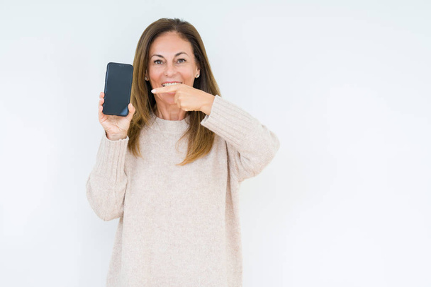 Mujer de mediana edad mostrando la pantalla del teléfono inteligente sobre fondo aislado muy feliz señalando con la mano y el dedo
 - Foto, imagen