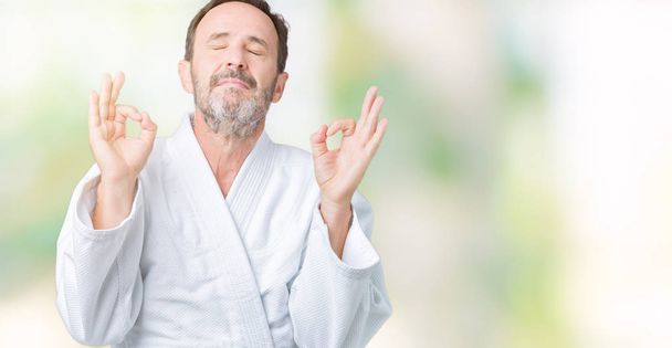 Komea keski-ikäinen vanhempi mies yllään kimono yhtenäinen yli eristetty tausta rentoutua ja hymyillen silmät kiinni tekee meditaatio ele sormin. Joogan käsite
. - Valokuva, kuva