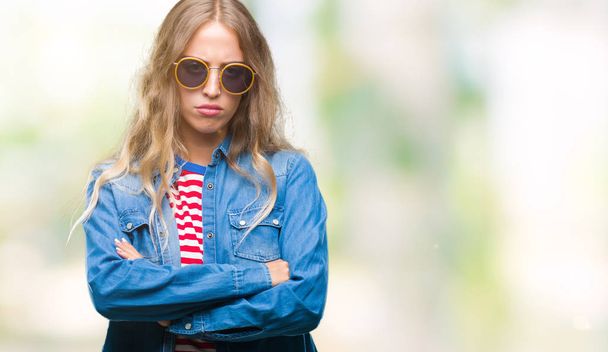 Beautiful young blonde woman wearing sunglasses over isolated background skeptic and nervous, disapproving expression on face with crossed arms. Negative person. - Photo, Image