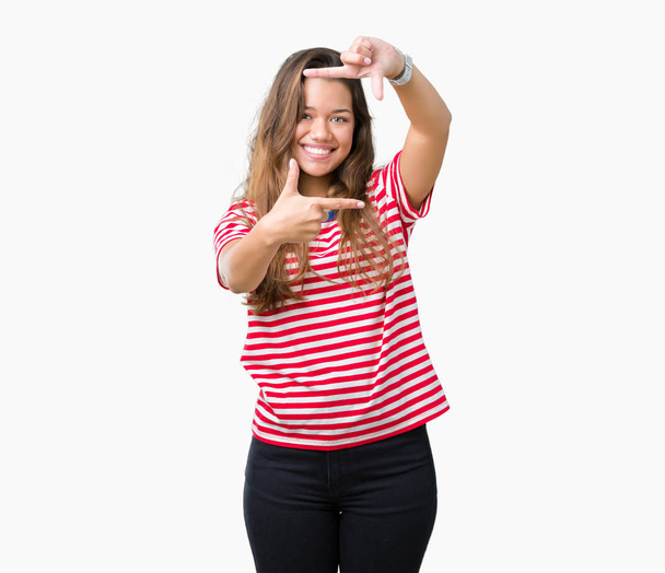 Young beautiful brunette woman wearing stripes t-shirt over isolated background smiling making frame with hands and fingers with happy face. Creativity and photography concept. - 写真・画像