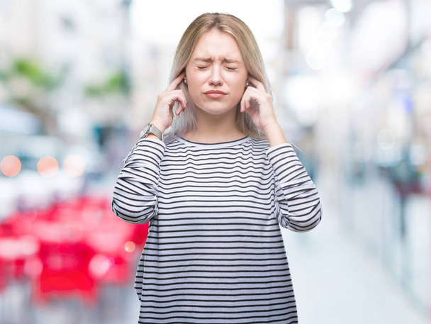 Mladá blond žena izolované pozadí pokrývající uši prsty s otrávený výraz pro hluk z hlasité hudby. Neslyšící koncepce. - Fotografie, Obrázek