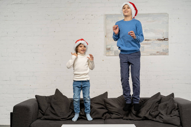 Two little brothers in santa hats having fun on sofa - Fotó, kép