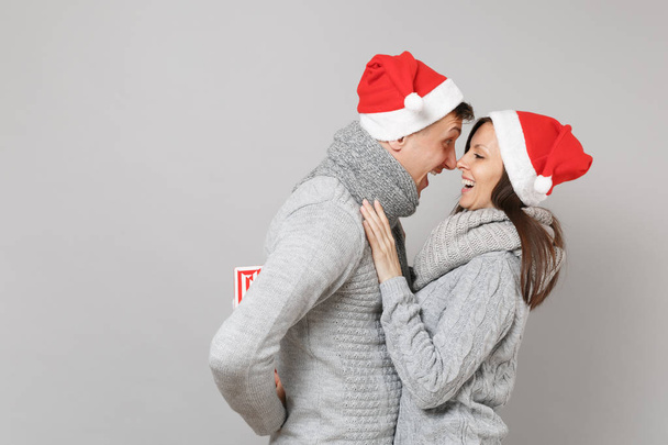 Merry fun couple girl guy in red Santa Christmas hat gray sweaters scarves isolated on grey wall background, studio portrait. Happy New Year 2019 celebration holiday party concept. Mock up copy space - Valokuva, kuva