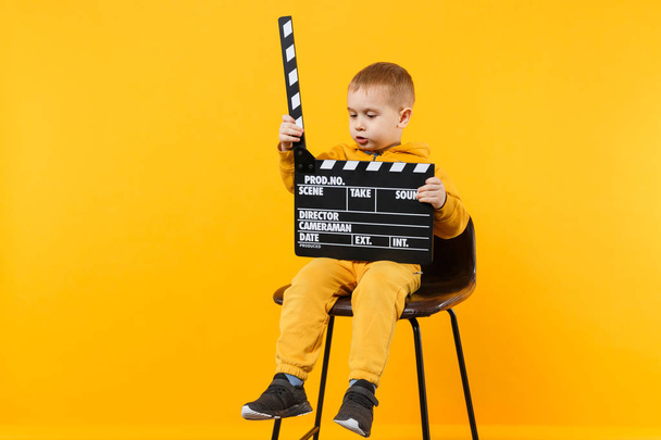 Little kid boy 3-4 years old in yellow clothes isolated on orange wall background, children studio portrait. People childhood lifestyle concept. Hand hold film making clapperboard. Mock up copy space - Foto, afbeelding
