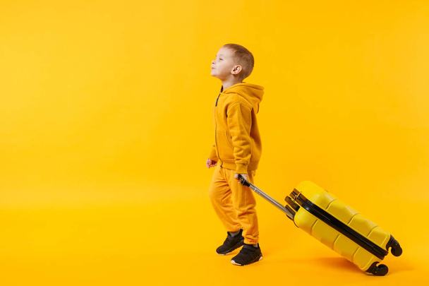 Little traveler tourist kid boy 3-4 years old isolated on yellow orange wall background studio. Passenger traveling abroad to travel on weekends getaway. Air flight journey concept. Mockup copy space - Photo, Image