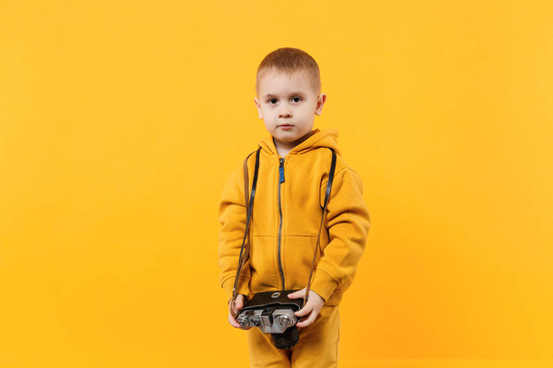 Little kid boy 3-4 years old wearing yellow clothes hold camera isolated on orange wall background, children studio portrait. People sincere emotions, childhood lifestyle concept. Mock up copy space - Photo, Image
