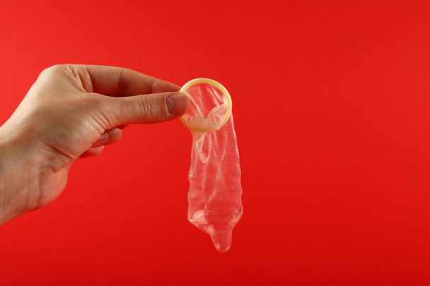 Close up man hand holding one open latex condom over red background with copy space, low angle side view - Foto, Imagen