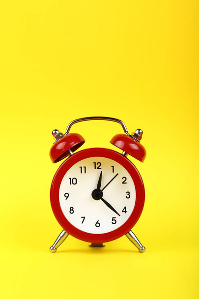 Cierre un pequeño reloj despertador retro de doble campana de metal rojo sobre fondo de papel amarillo con espacio para copiar, vista frontal de bajo ángulo - Foto, Imagen