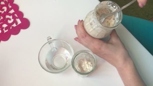 A woman mixes fermented sourdough bread. On the table are the ingredients for feeding bread sourdough. Flour and water. - Video