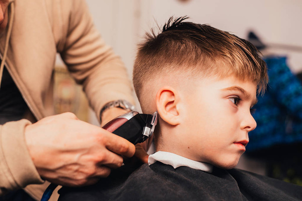 cropped image of barber making haircut of little boy at salon - Foto, Bild