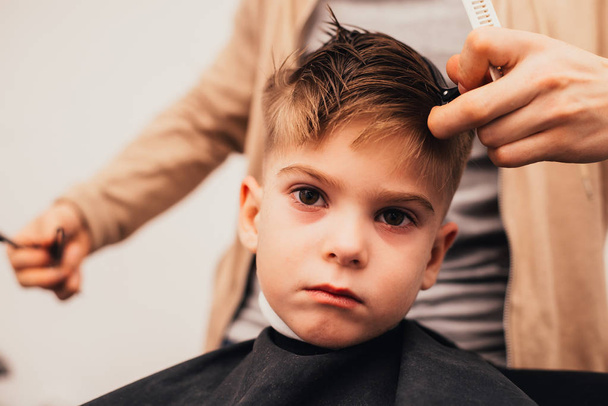 cropped image of barber making haircut of little boy at salon - Фото, изображение