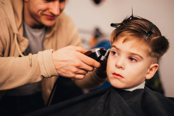 cropped image of barber making haircut of little boy at salon - Photo, image