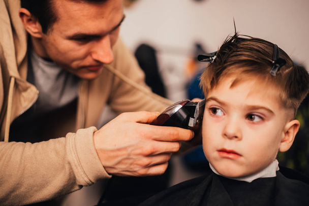cropped image of barber making haircut of little boy at salon - Foto, imagen